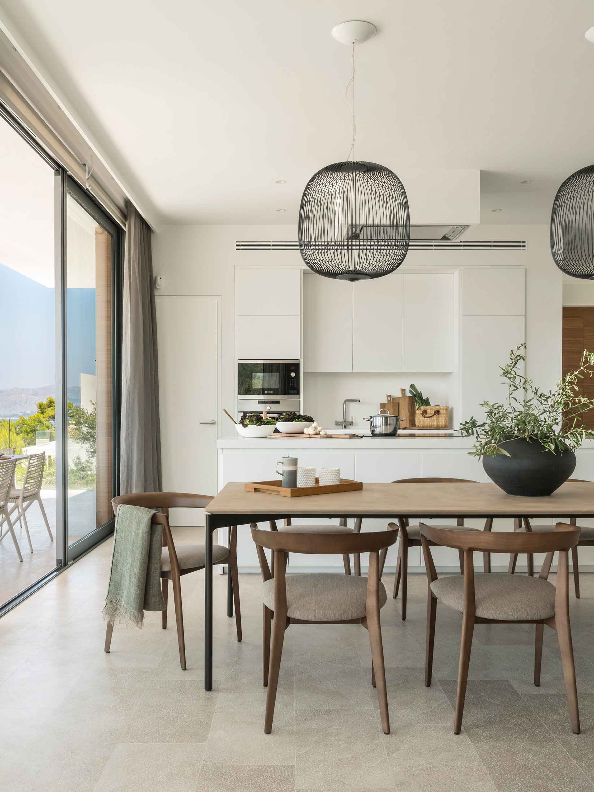 Dining area and kitchen with large sliding window open to the terrace and pale stone floor