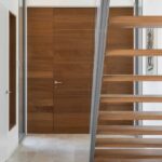 Entrance hall with flush-fitted timber door, pale stone floor and staircase with timber treads