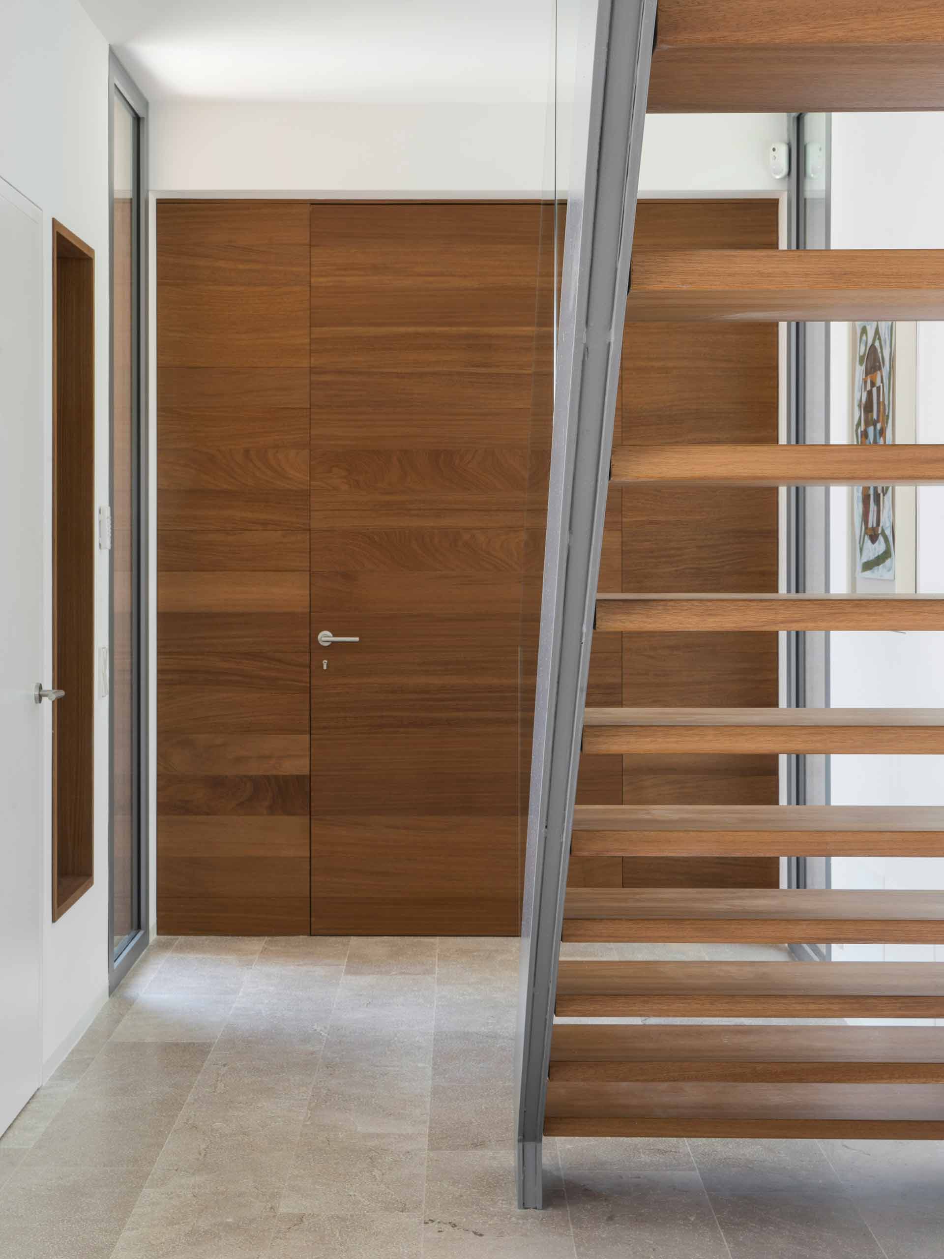 Entrance hall with flush-fitted timber door, pale stone floor and staircase with timber treads