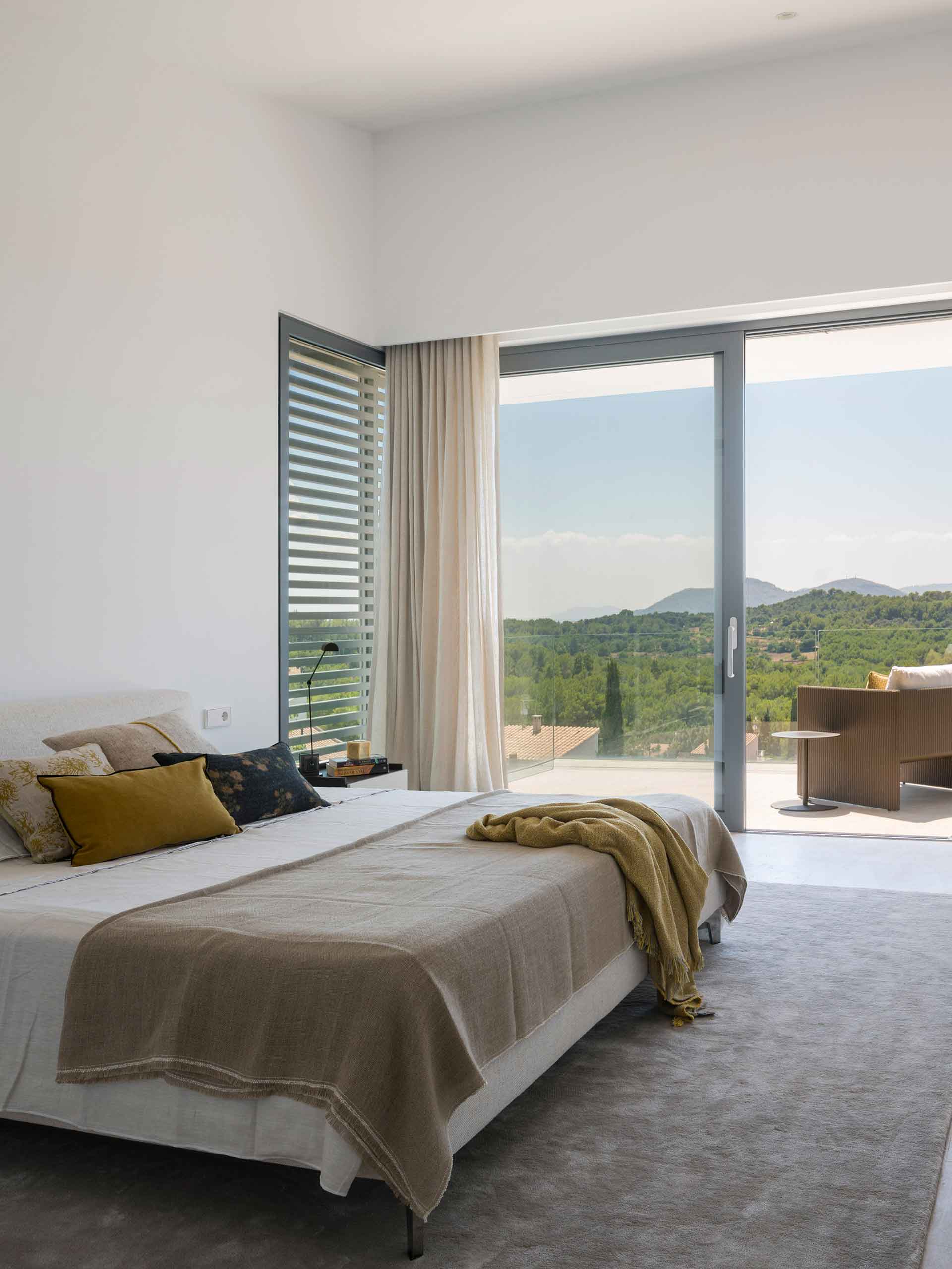 Bedroom with beige bedspread, mustard throw and sliding door to a terrace with views of the hills