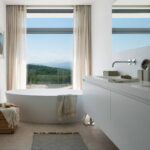 Bathroom with oval freestanding bath in front of a large window with hill views and wall-hung basin