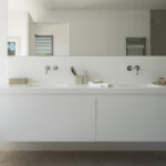 Bathroom with white wall-hung double basin, large mirror, concealed taps and stone floor