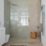 Level-access shower with glass screen, veined cladding in sand tones and heated towel rail