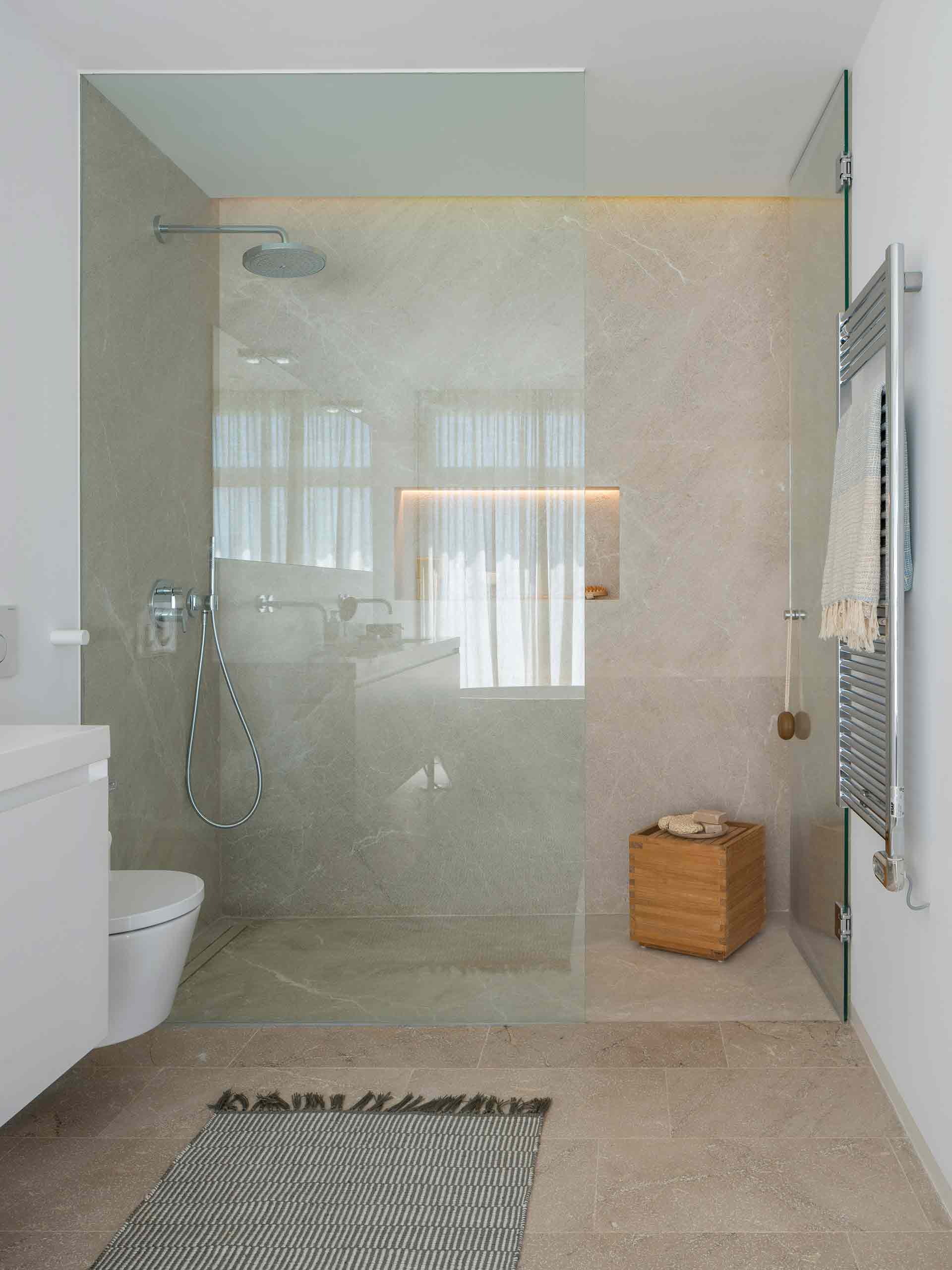 Level-access shower with glass screen, veined cladding in sand tones and heated towel rail