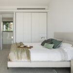 Bedroom with white built-in wardrobe, bed with beige headboard, green cushions and colourful paintings