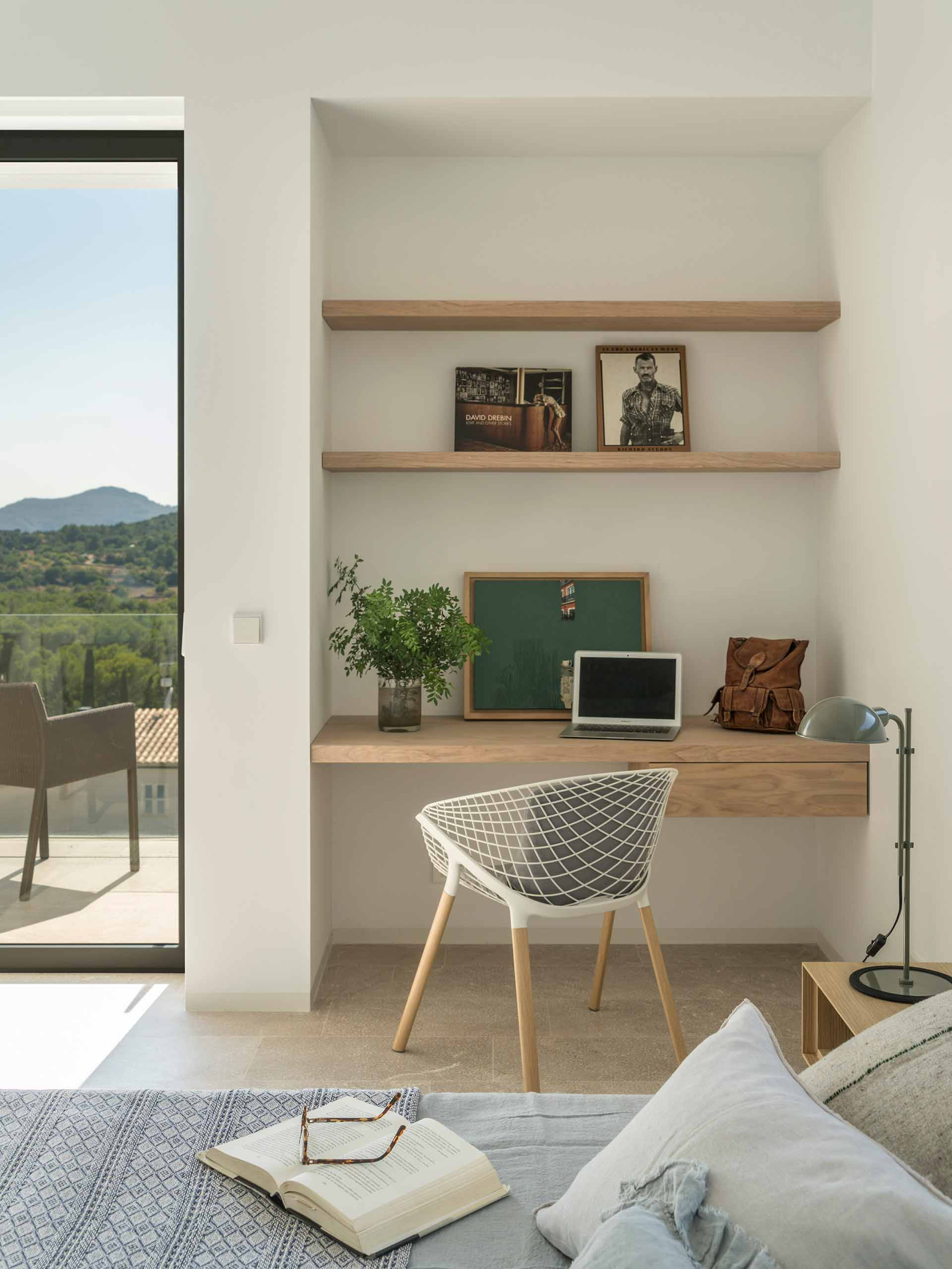 Desk built into a niche with wooden shelves, white cane chair and mountain views