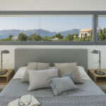 Grey headboard between two floating wooden bedside tables, with a horizontal window overlooking the sea