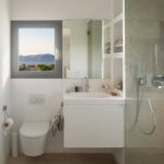 Bathroom with window and sea views, wall-hung toilet, white basin and glazed shower
