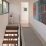 Upper-floor landing with open staircase, glass balustrade, abstract paintings and rug