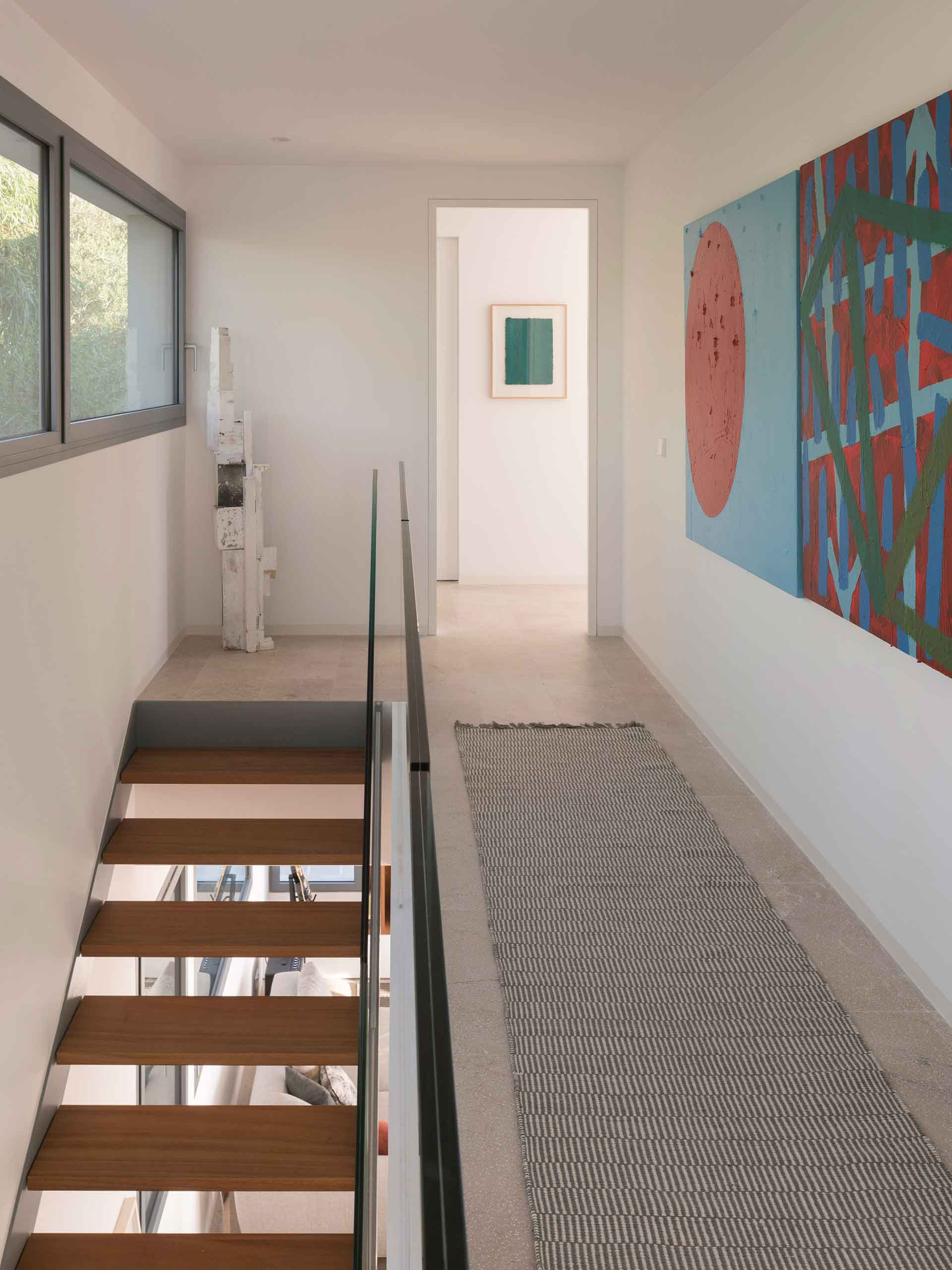 Upper-floor landing with open staircase, glass balustrade, abstract paintings and rug