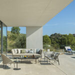 Covered terrace with beige sofa, armchair, large glass windows onto the living room and pool on the right