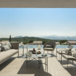 Coffee table with fruit and outdoor sofa on pale stone, with the sea behind the pool