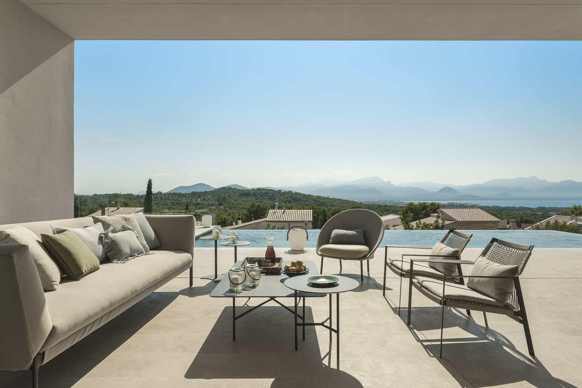 Coffee table with fruit and outdoor sofa on pale stone, with the sea behind the pool