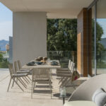 Outdoor dining area under the overhang with long table, woven rope chairs and green armchair