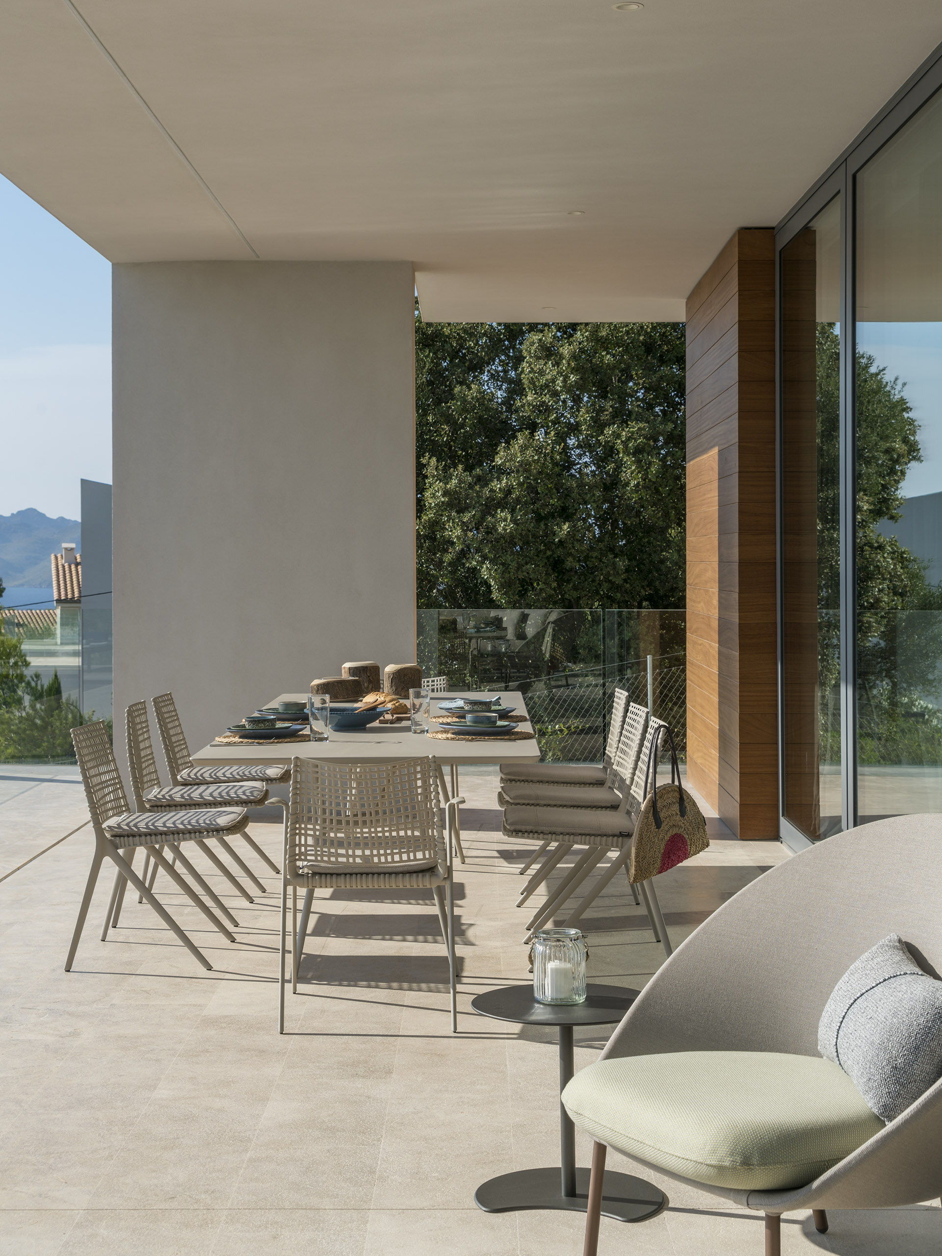 Outdoor dining area under the overhang with long table, woven rope chairs and green armchair