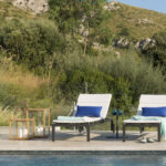 Sun loungers with blue cushions and wooden lanterns beside the pool, with a hillside behind