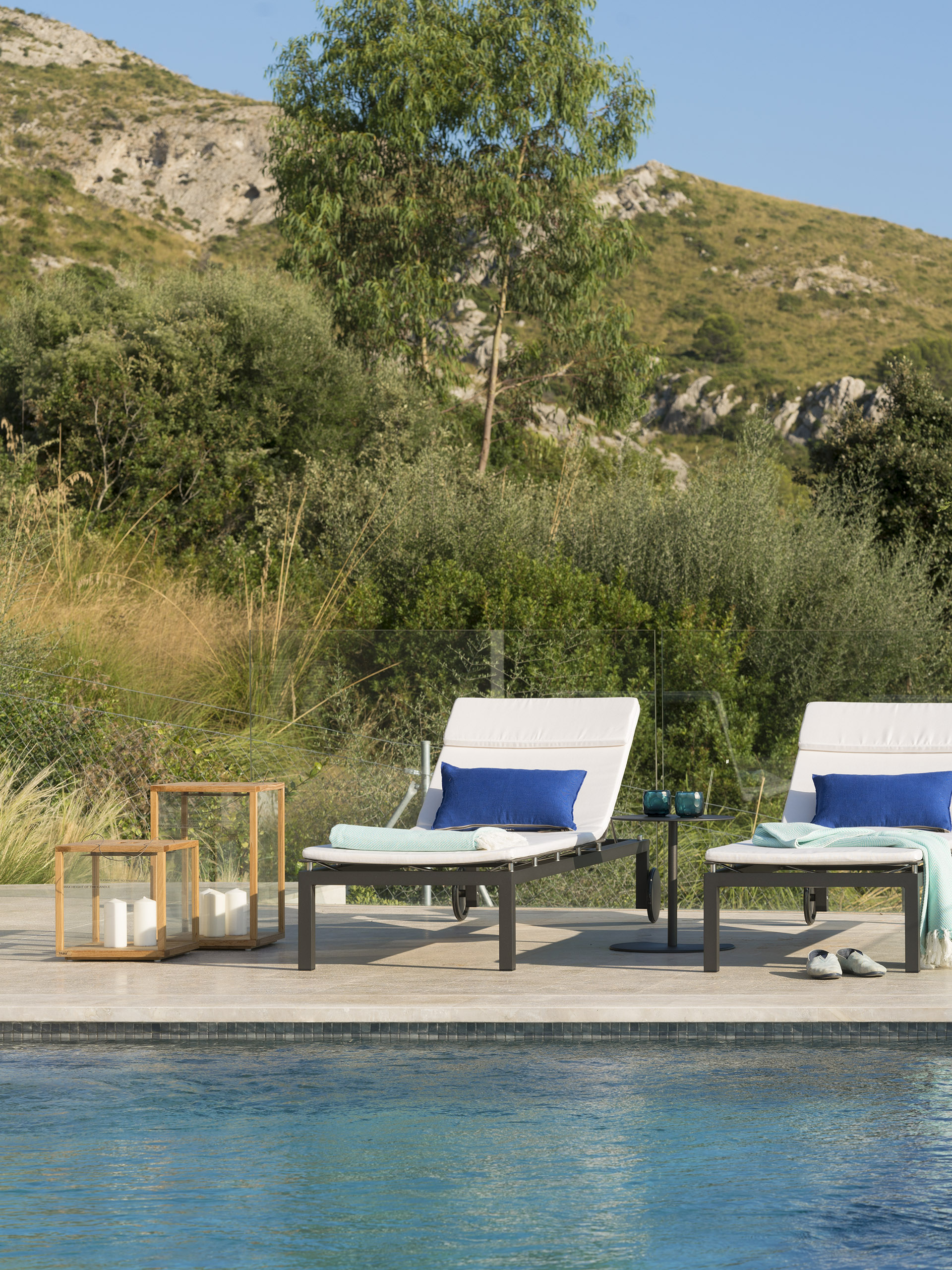 Sun loungers with blue cushions and wooden lanterns beside the pool, with a hillside behind