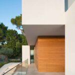 Covered entrance with timber-clad wall, white overhang, glass balustrade and pale stone floor