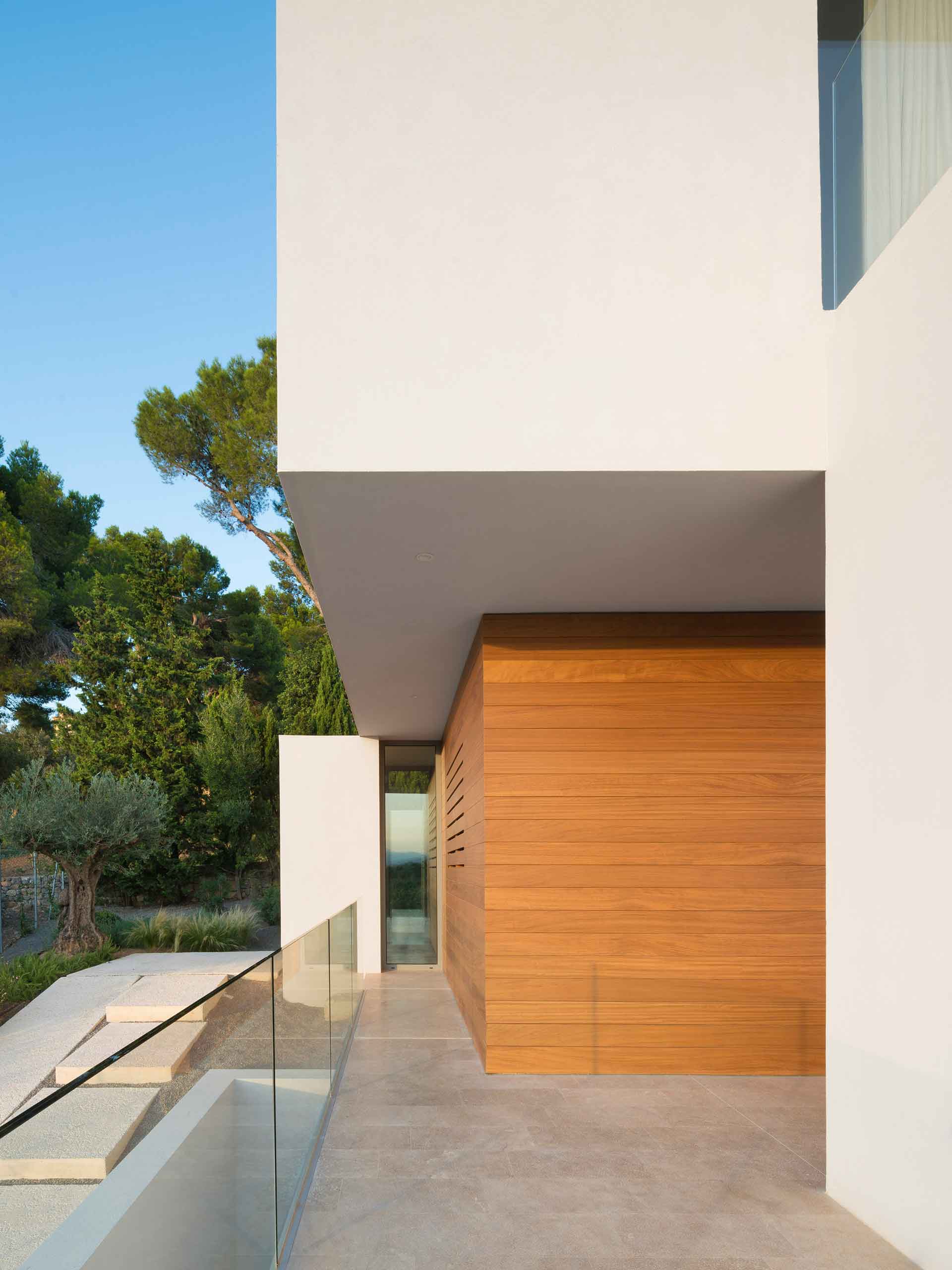Covered entrance with timber-clad wall, white overhang, glass balustrade and pale stone floor
