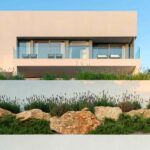 Upper volume of the house with glass balcony above a terraced garden with rocks and lavender