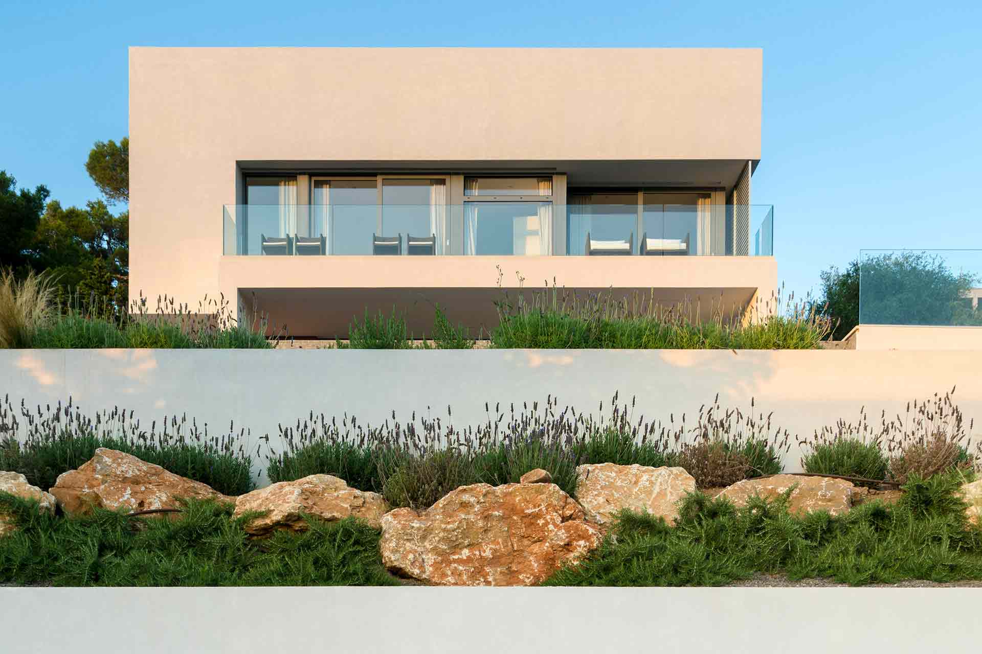Upper volume of the house with glass balcony above a terraced garden with rocks and lavender