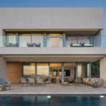 Front view at dusk of the two-storey house with warm light and swimming pool