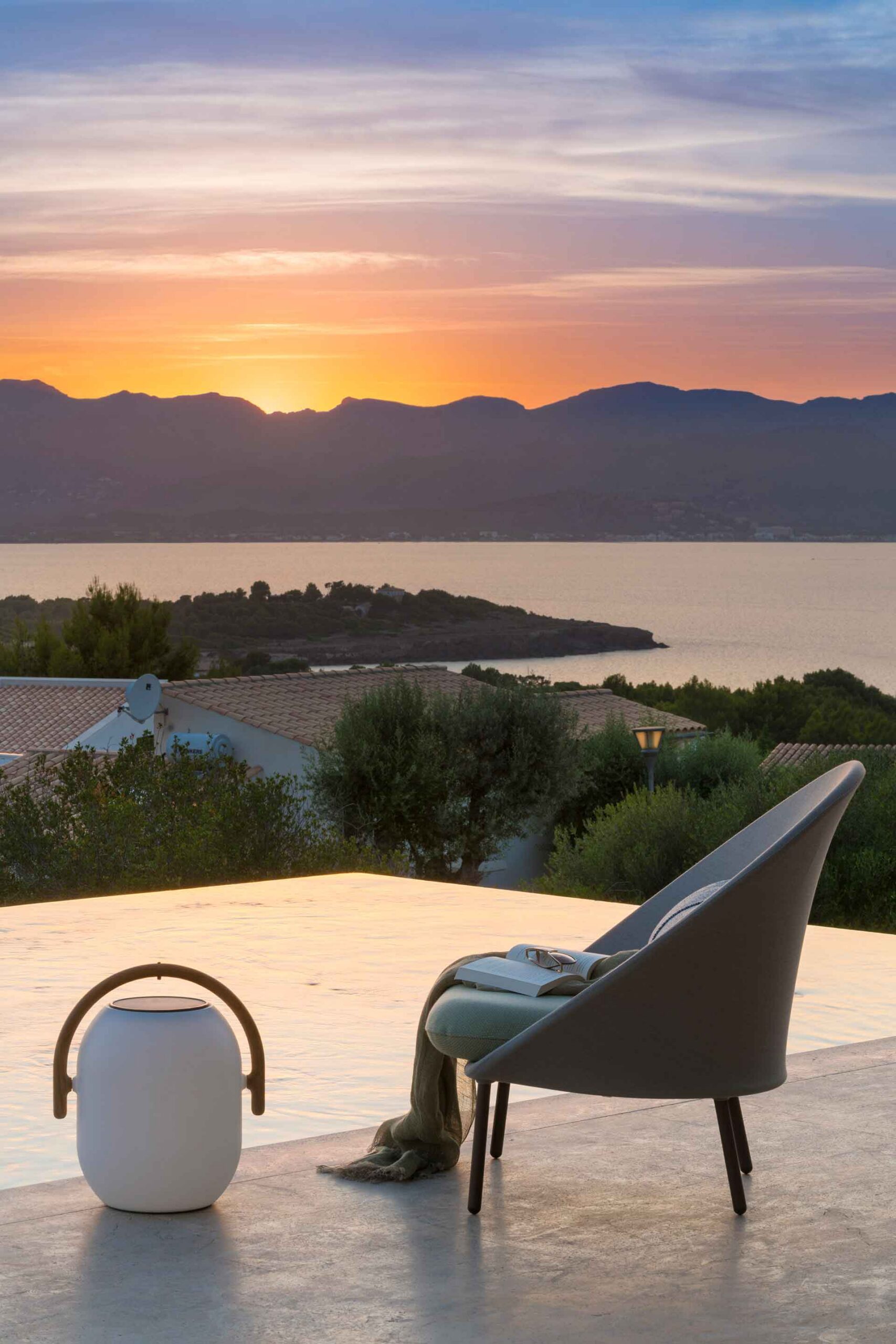Sunset with armchair, open book and portable lamp beside the edge of the infinity pool