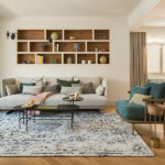 Wohnzimmer des Projekts Horts mit hellem Sofa, eingebautem Eichenregal, petrolblauem Sessel und Fischgrätparkett