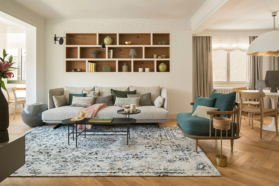 Salón del proyecto Horts con sofá claro, estantería empotrada de roble, sillón azul petróleo y parqué en espiga