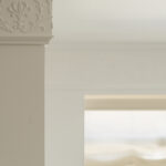 Detail einer klassischen Stuckprofilierung mit Blumenrelief an einer weißen Säule, mit weichem Licht im Hintergrund
