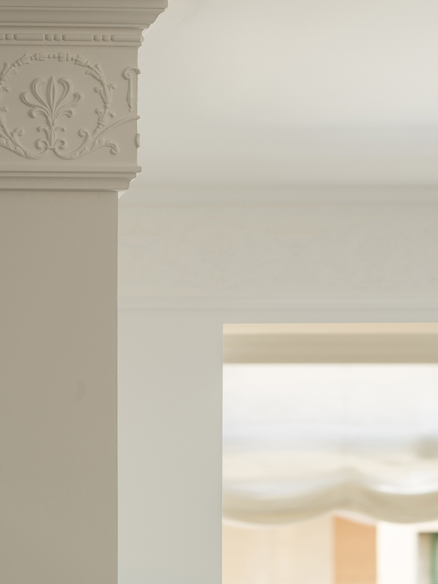 Detail einer klassischen Stuckprofilierung mit Blumenrelief an einer weißen Säule, mit weichem Licht im Hintergrund