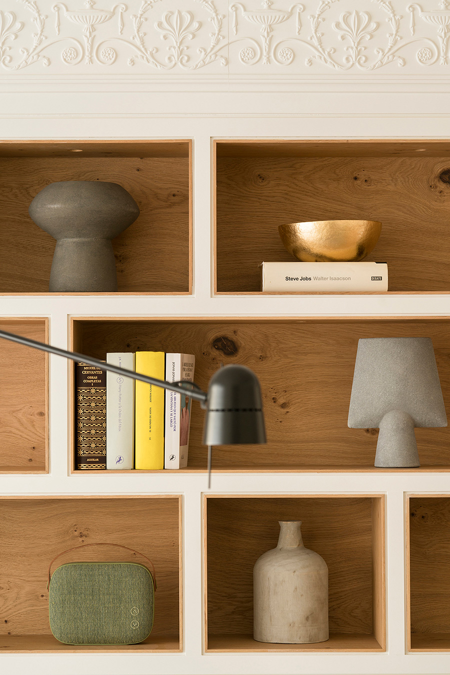 Detalle de la estantería empotrada con fondo de roble, cerámicas grises, libros y cornisa de escayola decorada