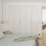 Schlafzimmer mit zartgrüner Tagesdecke und grauem Plaid, offene Tür zum Flur und weiterer Raum im Hintergrund