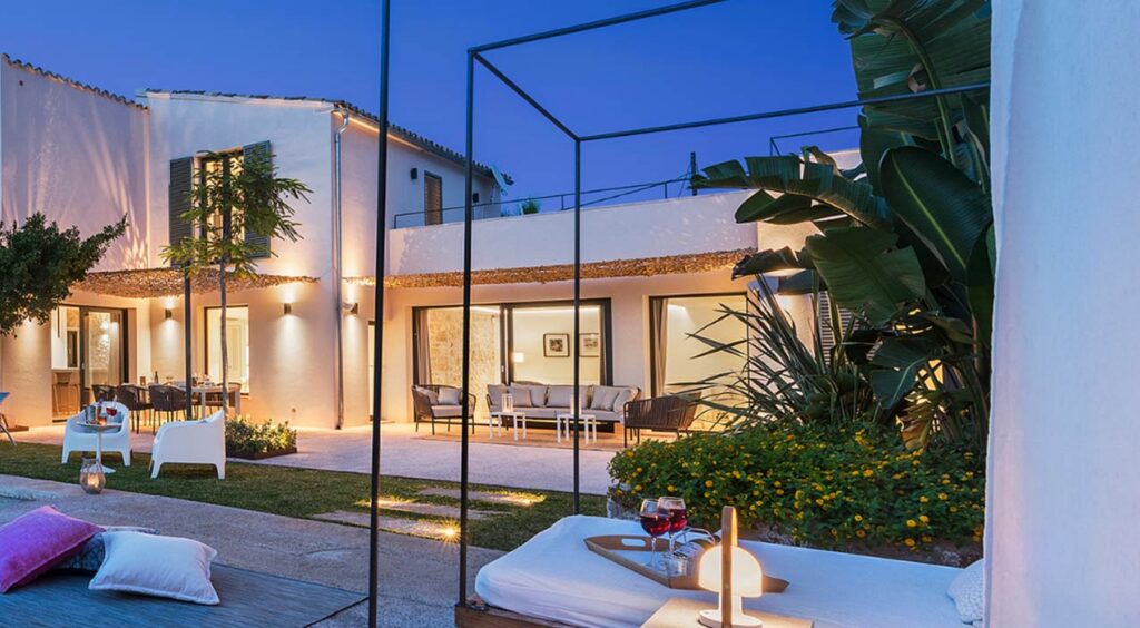 Villa Pollentia al anochecer con fachada blanca, salón exterior iluminado, jardín y cama balinesa