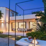 Villa Pollentia al anochecer con fachada blanca, salón exterior iluminado, jardín y cama balinesa