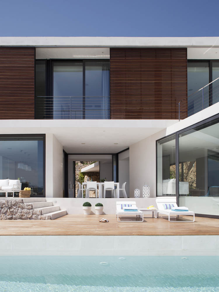 Zweigeschossige Fassade mit Holzgitter, Terrasse mit Holzdeck, Sonnenliegen und Pool im Vordergrund