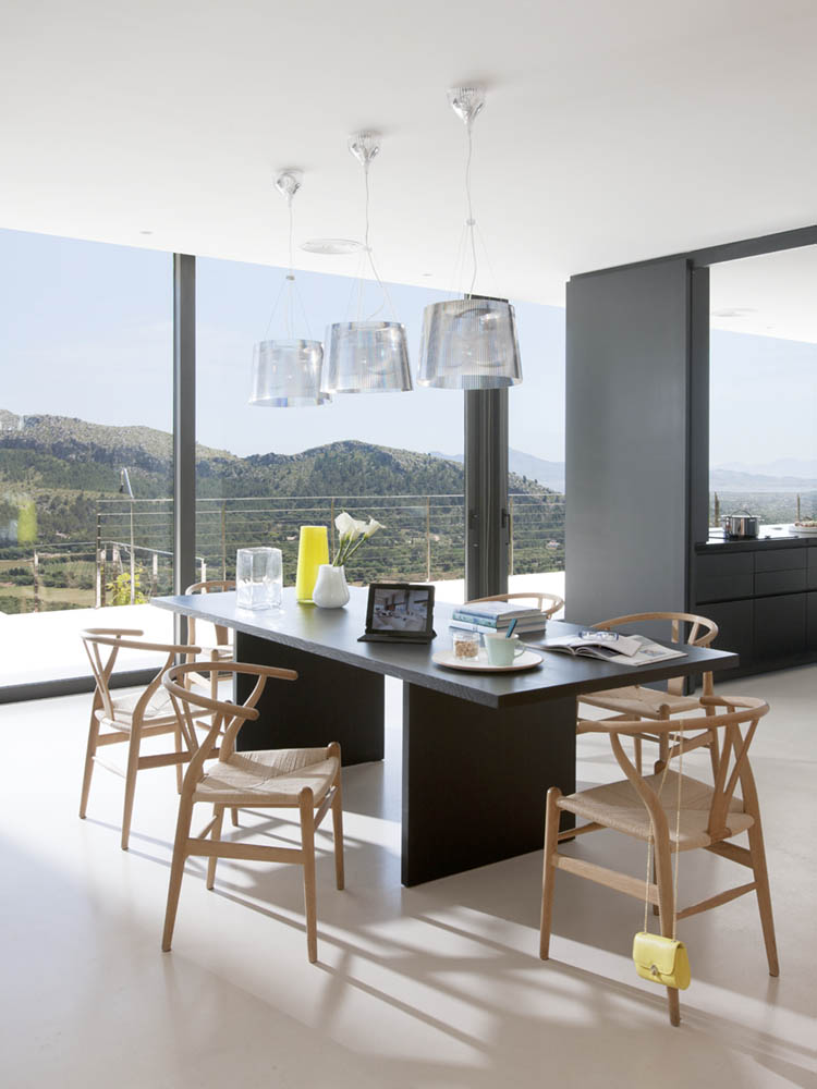 Esszimmer mit dunklem Tisch, Holzstühlen und Pendelleuchten vor großen Fenstern mit Blick auf die Berge