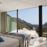 Schlafzimmer mit raumhohem Fenster und Terrasse mit Blick auf Berge und Meer