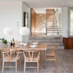 Detalle vertical del comedor: lámparas esféricas colgantes, sillas de madera y escalera con pared de piedra al fondo
