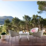 Terraza con suelo de madera, sillas blancas de diseño y vistas a pinos y montaña