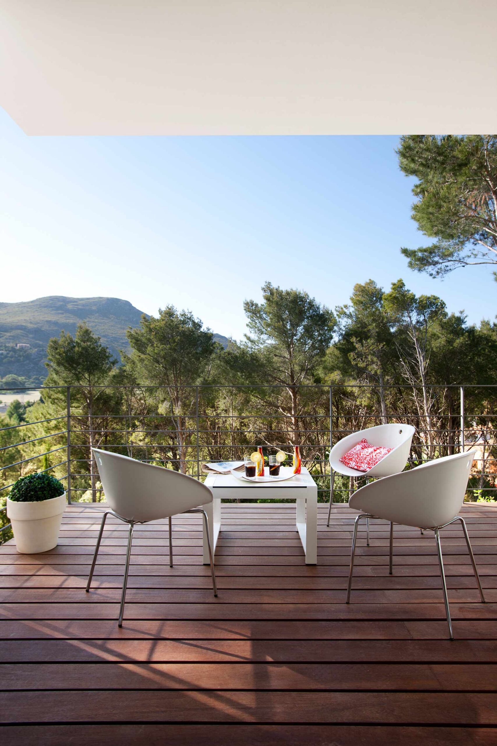 Terraza con suelo de madera, sillas blancas de diseño y vistas a pinos y montaña