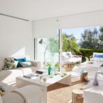 Sofa mit gemusterten Kissen, Stehlampe und großem Schiebefenster mit Rollos zum Garten