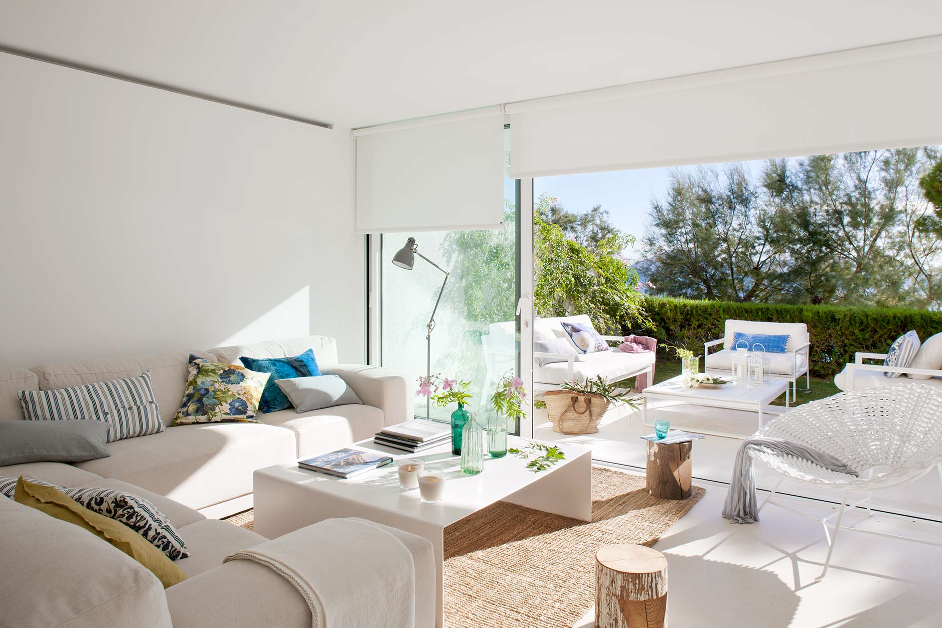 Sofa mit gemusterten Kissen, Stehlampe und großem Schiebefenster mit Rollos zum Garten