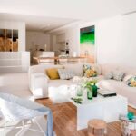 Offener Wohnraum mit cremefarbenem Sofa und Juteteppich, dahinter Essbereich und Küche, ein Strandbild