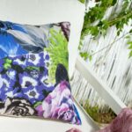 Geblümtes Kissen in Blau, Violett und Grün auf weißem Sessel, mit rosa Decke und Schilfzaun