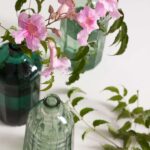 Nahaufnahme von Zweigen mit rosa Blüten vor grünen Glasflaschen in zwei Farbtönen