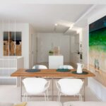 Esstisch aus Holz mit weißen Stühlen hinter dem Sofa, dahinter Küche mit Insel