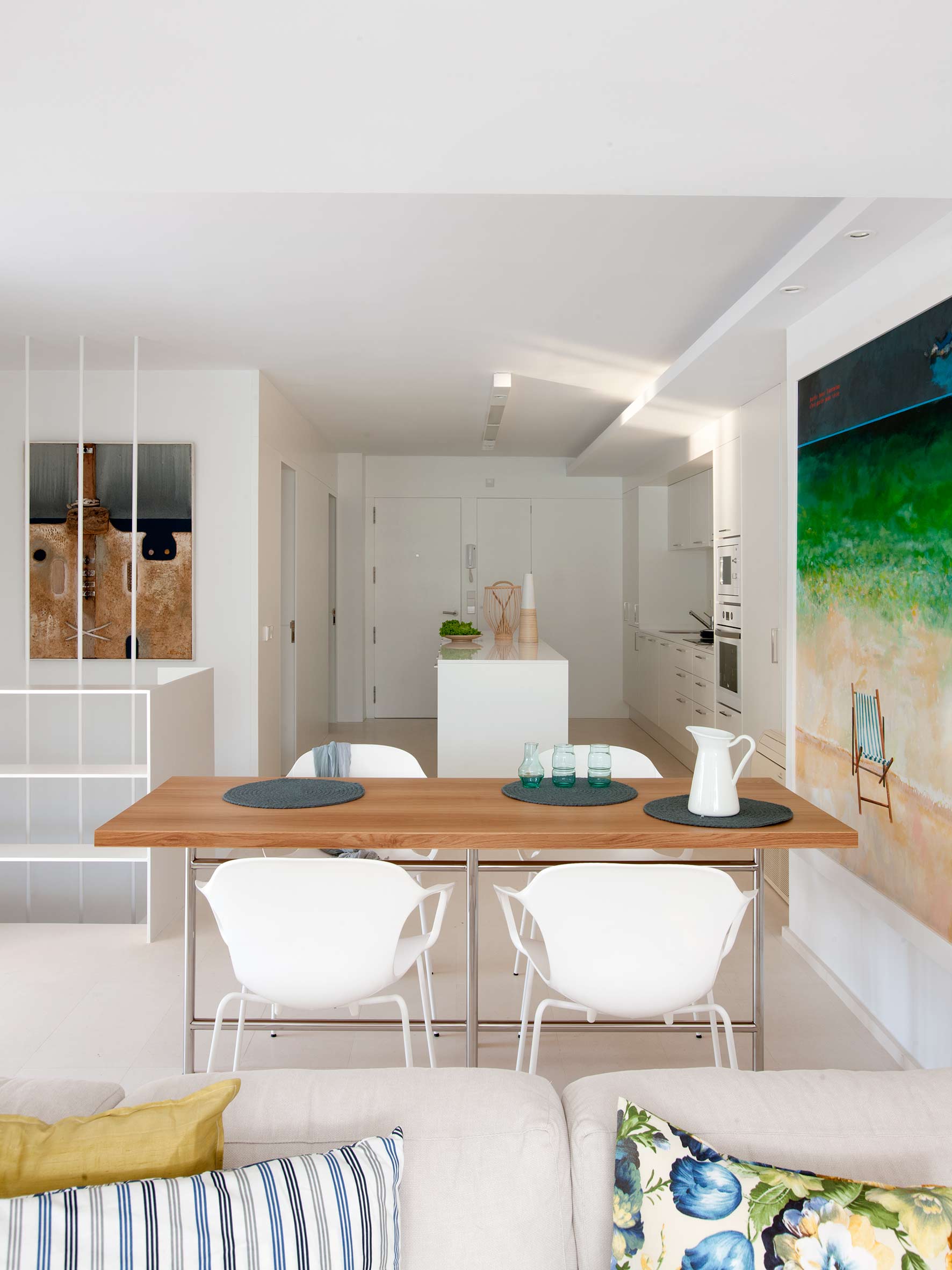 Esstisch aus Holz mit weißen Stühlen hinter dem Sofa, dahinter Küche mit Insel