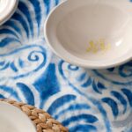 Detail eines blau-weißen Tischtuchs mit heller Keramikschale und Untersetzer aus geflochtener Faser