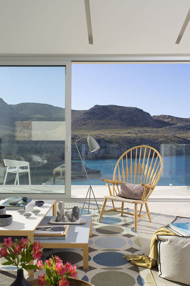 Butaca de madera y lámpara de pie ante un ventanal corredero con vistas a la cala